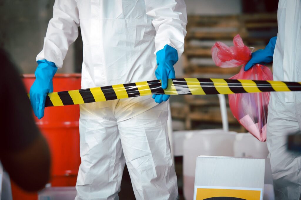 Hazardous waste cleanup workers in protective suits and gloves setting up caution tape and handling biohazard materials